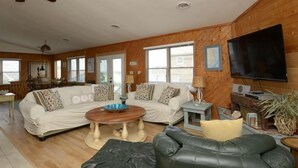 A spacious living room with a wooden interior, a large flat-screen TV, and a dining area with a table and chairs.