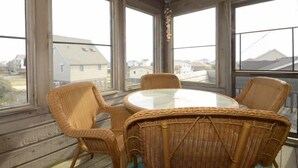 A room with wicker furniture, large windows, and a view of houses.