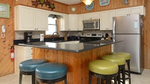 A kitchen with wooden paneling, white cabinets, a stainless steel refrigerator, a microwave, and a large island with stools.