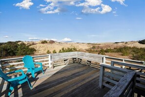 A wooden deck with two turquoise Adirondack chairs facing a sandy landscape under a clear sky. - Historic old Nags Head next to Jockey's Ridge! Great views, walk to sound access (Nags Head)