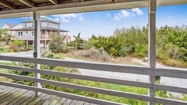 A wooden deck with a view of a two-story house and surrounding vegetation. - Old Nags Head style with wrap around porch! Soundside Rd in Nags Head! (Nags Head)