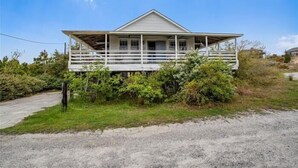 A two-story house with a porch, surrounded by greenery. - Old Nags Head style with wrap around porch! Soundside Rd in Nags Head! (Nags Head)