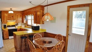 Una cocina con armarios de madera, una encimera amarilla, una mesa redonda de vidrio y sillas, y una lámpara colgante.