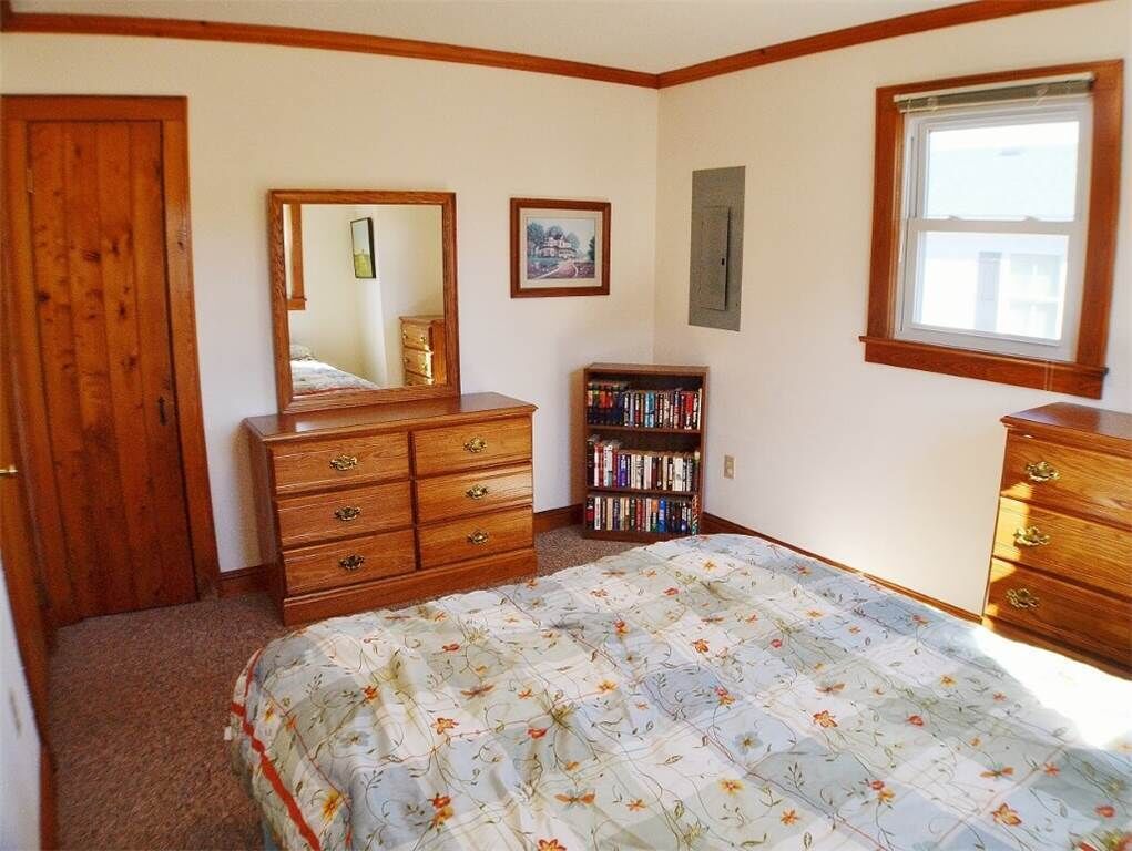 Un dormitorio con cama, cómoda de madera, estantería, espejo y ventana.
