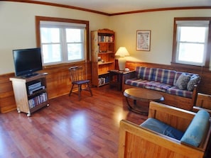 A living room with a television, bookshelves, a sofa, and a lamp. - Just blocks from the beach on a budget! Nostalgic 3 BR cottage in Nags Head! (Nags Head)