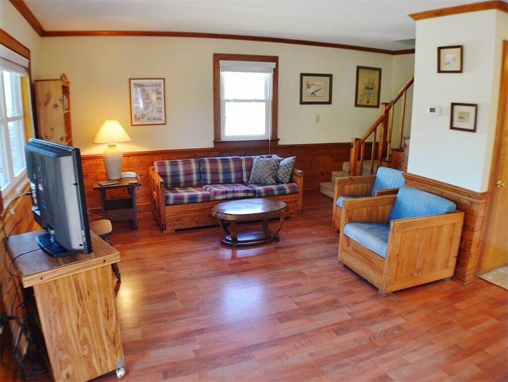 Una sala de estar con piso de madera, un sofá a cuadros, un sillón azul, una mesa de centro y un televisor sobre un mueble de madera.