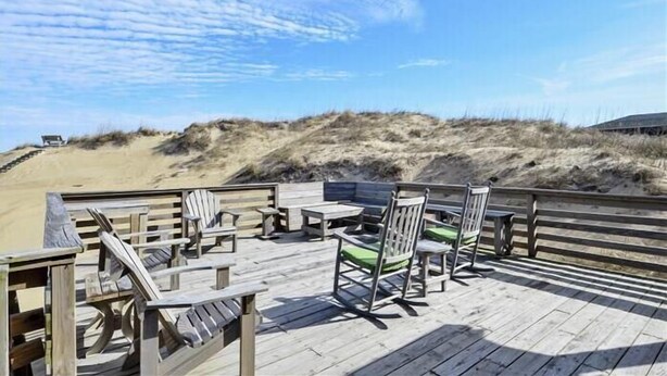 A wooden deck with outdoor seating, overlooking a sandy beach and dunes. - Classic Outer Banks style oceanfront home in Kill Devil Hills! (Kill Devil Hills)