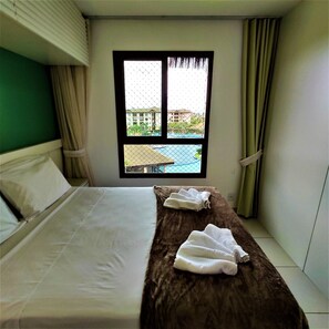 A hotel room with a bed, a window with a view of buildings, and a curtain. - VG Sun Cumbuco Studio By DM Apartments (Caucaia)