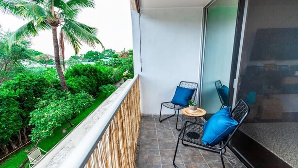 Een balkon met twee stoelen, een kleine tafel en een groot raam met uitzicht op een weelderige tuin.