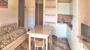 Un ambiente compatto con un tavolo da pranzo, sedie, un divano, angolo cottura e TV.