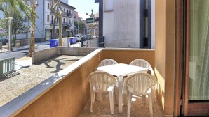 Un balcone con tavolo e sedie bianche, un muro in cemento e vista sulla strada.