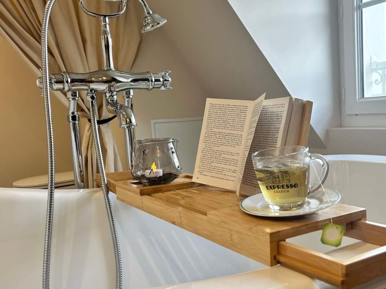 A bathroom with a bathtub, a glass of coffee, and a book on a wooden tray.