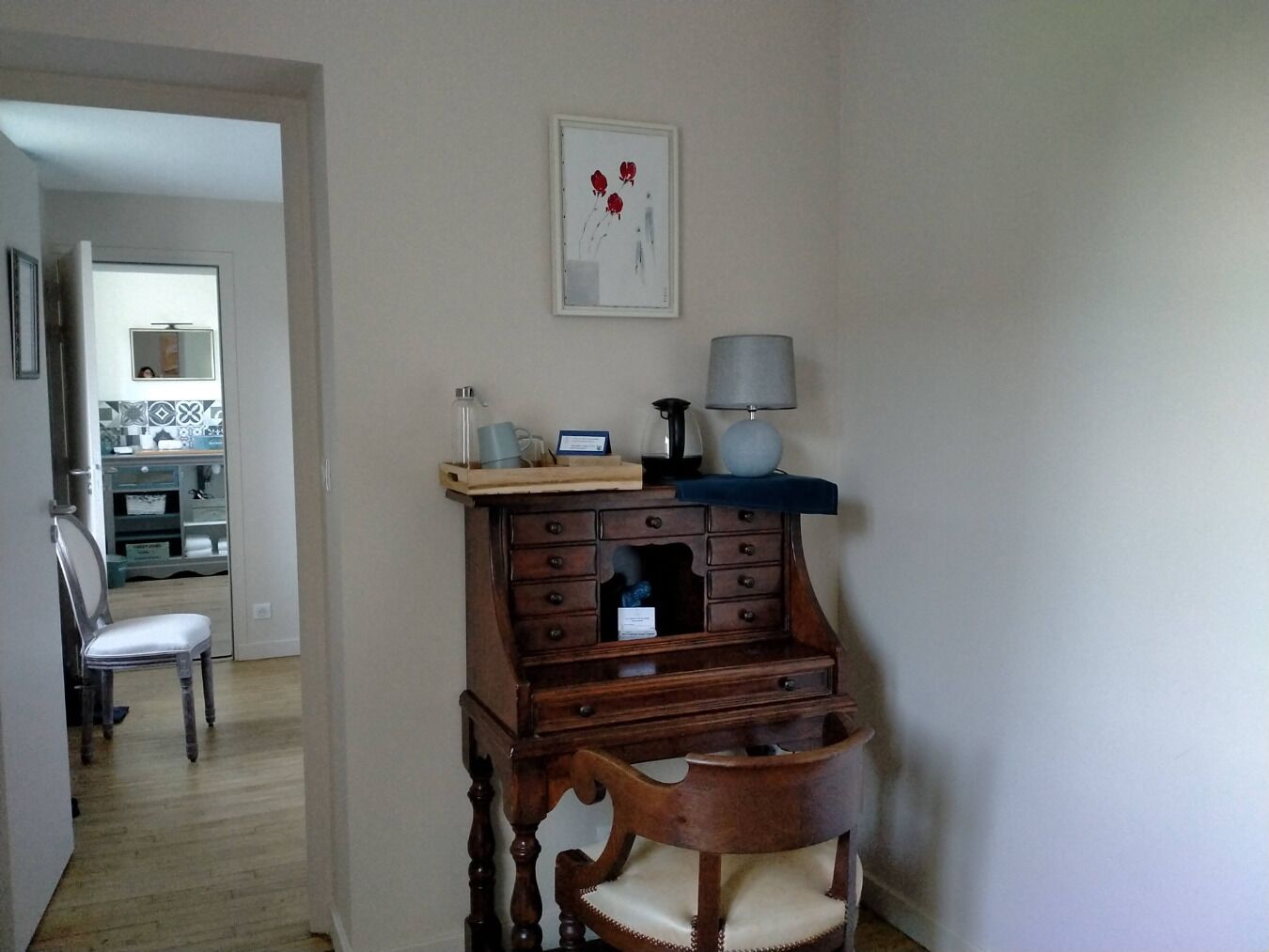 A wooden desk with drawers, a chair, and a lamp. A framed picture hangs on the wall above the desk.