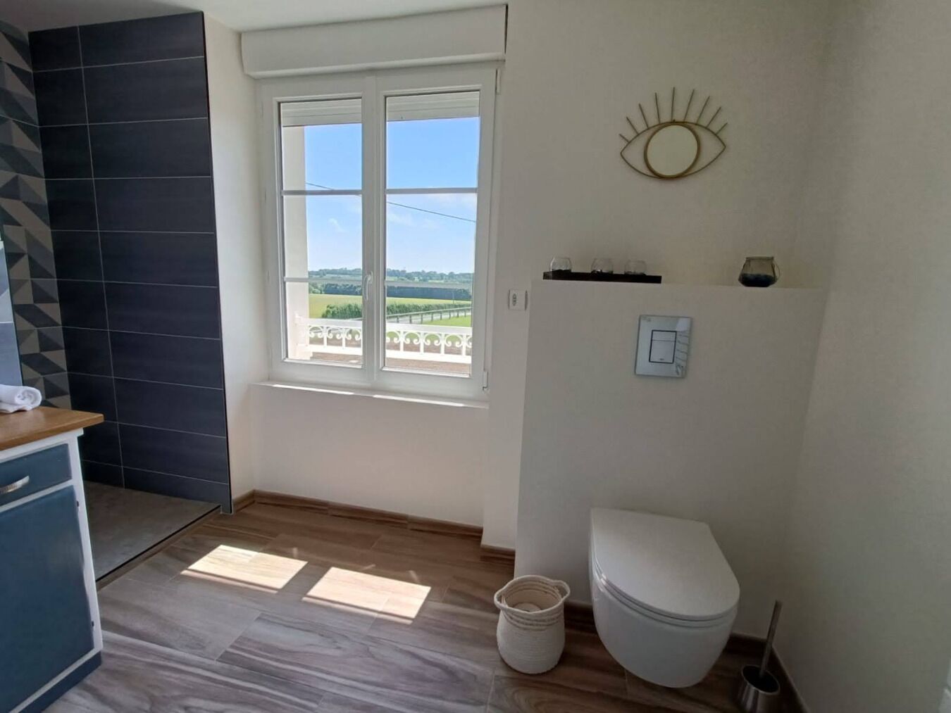 A bathroom with a toilet, a bidet, a sink, and a window with a view of the countryside.