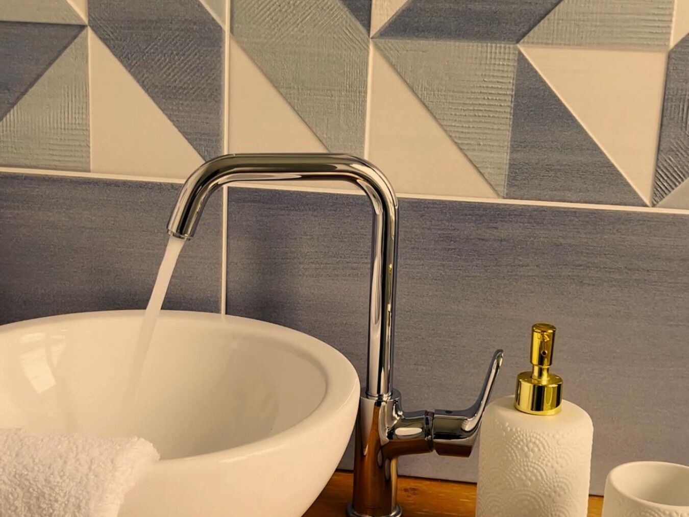 A bathroom with a white sink, chrome faucet, and a gold soap dispenser.