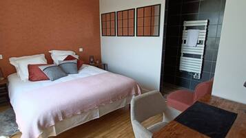 A bedroom with a bed, bedside tables, a chair, a small table, and a wall-mounted towel rack.