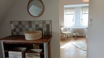 Une salle de bain avec un meuble-lavabo en bois, un miroir rond et un pare-feu en carreaux.
