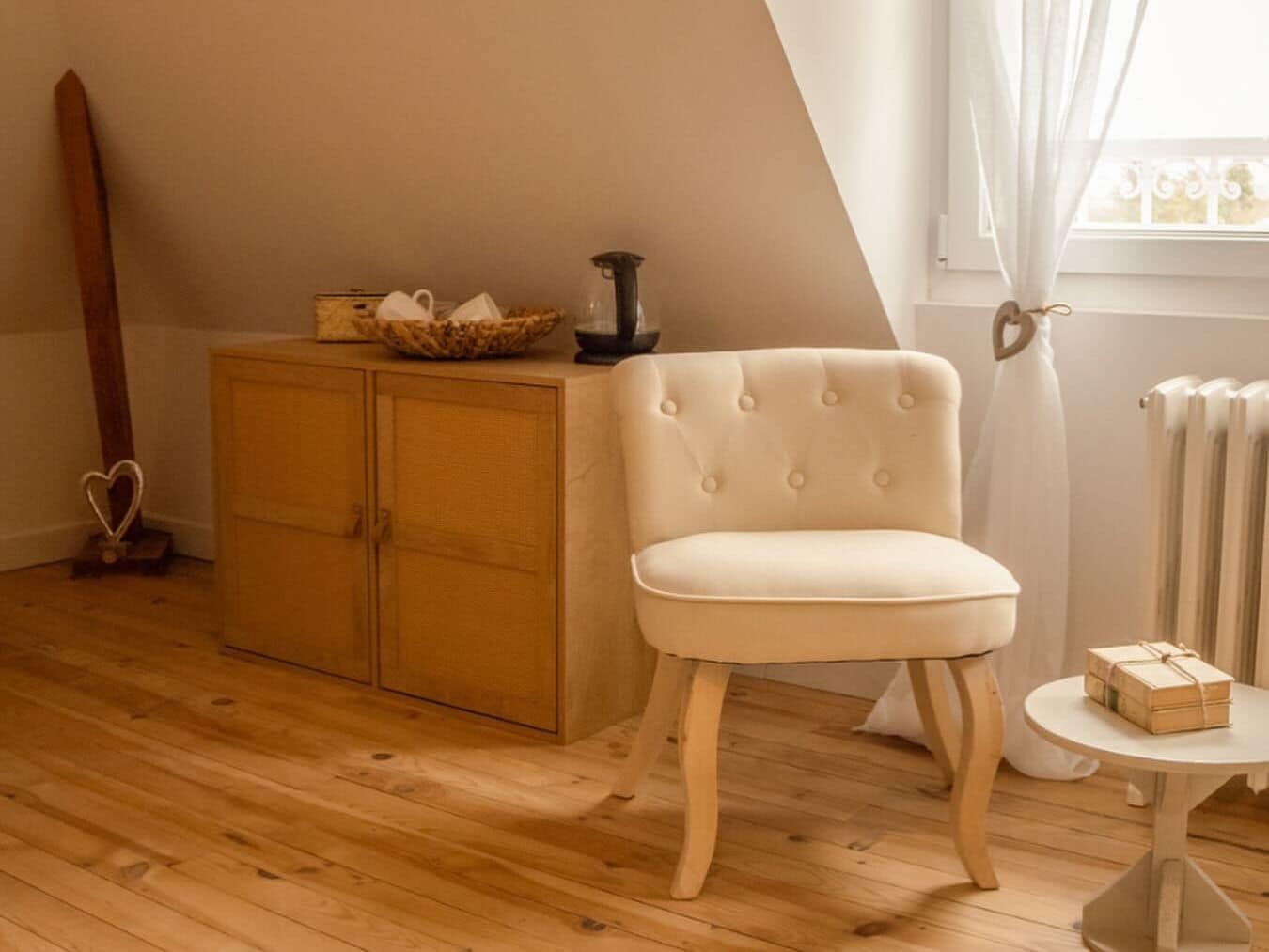 Et værelse med trægulv, en beige polstret stol, et træskab og en radiator.
