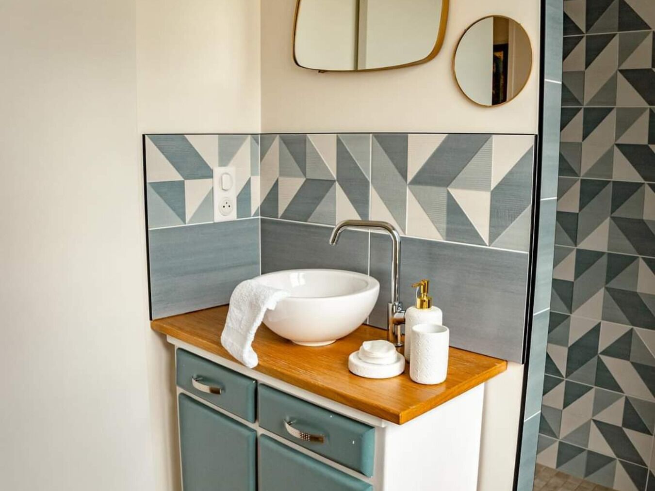 A bathroom with a white sink, wooden countertop, teal cabinets, and geometric patterned tiles.