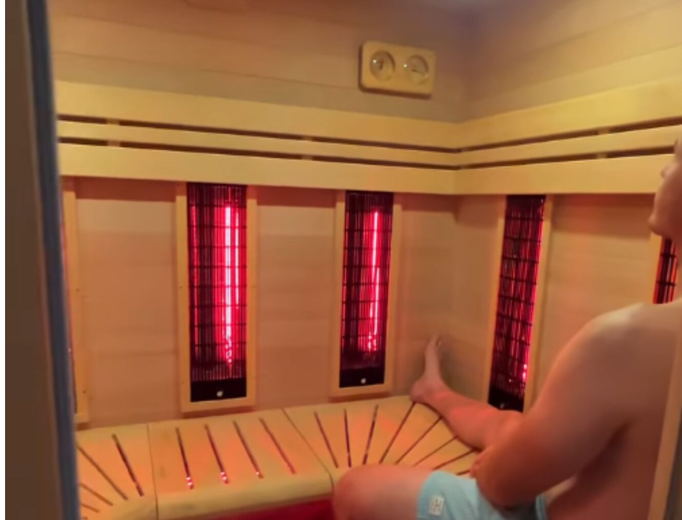 A sauna room with a wooden bench, red-tinted windows, and a control panel on the wall.