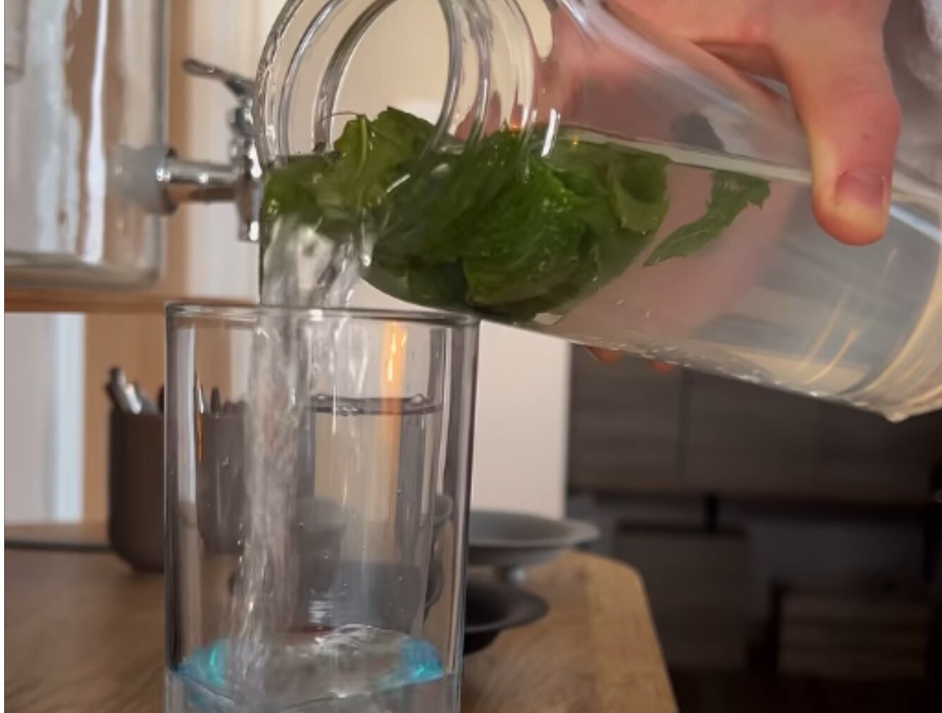 A hand pouring water from a glass pitcher into a clear glass.