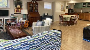 A spacious living room with a sofa, a coffee table, a bookshelf, a guitar, and a dining area with a table and chairs.