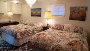 A bedroom with two beds, a chandelier, a painting, and a window.