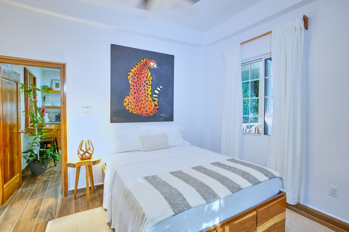 Un dormitorio con una cama, un cuadro de un guepardo, una ventana con cortinas y una planta.
