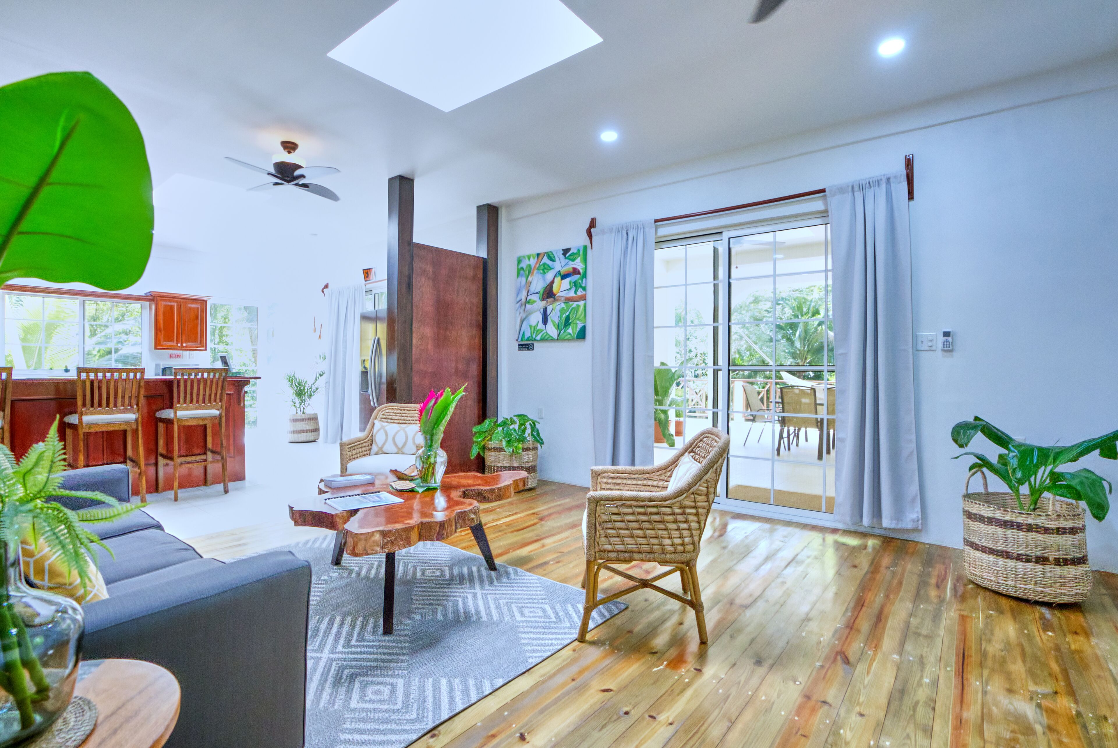 Amplia sala de estar con piso de madera, un sofá, una mesa de comedor con sillas y un ventanal con cortinas.