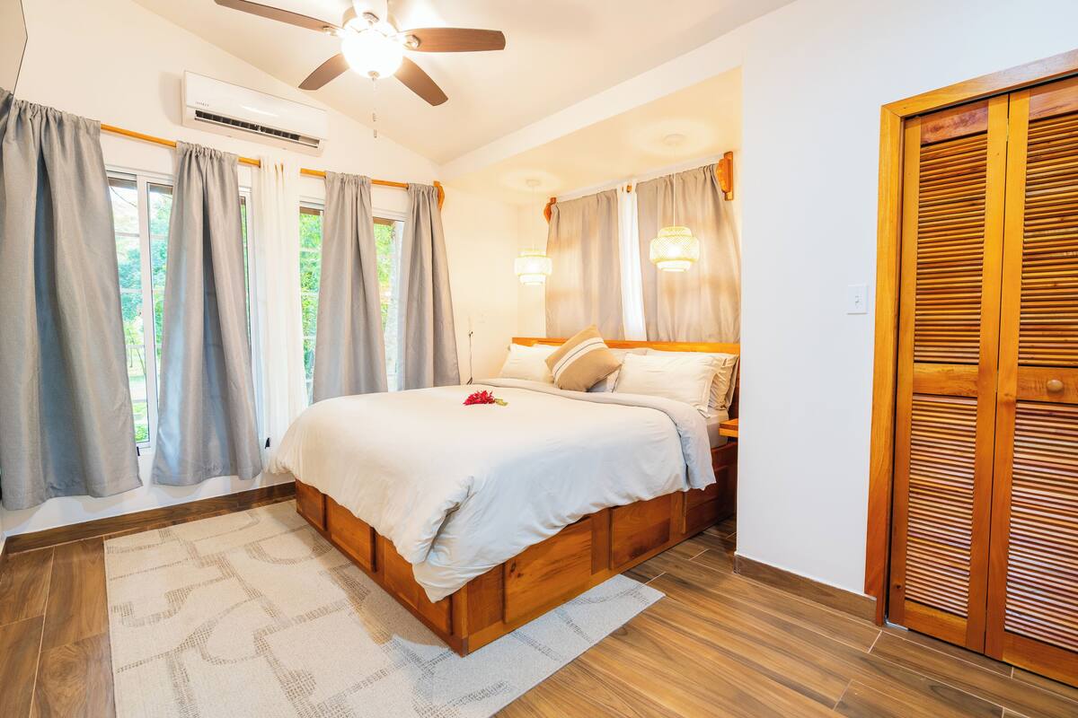 Un dormitorio con cama, cortinas, ventilador de techo y armario de madera.