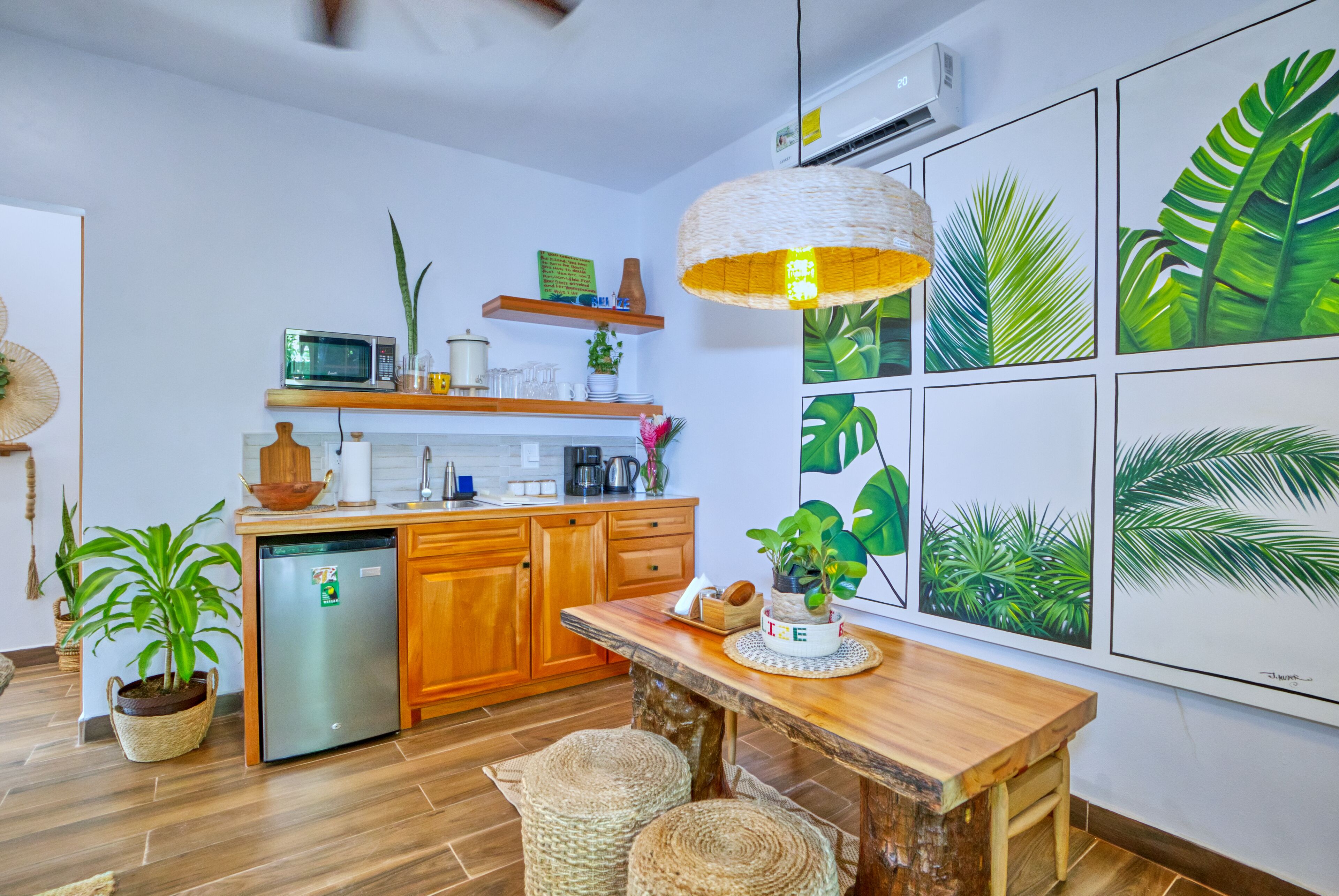 A modern kitchen with wooden cabinets, a built-in microwave, and a refrigerator. There are several potted plants and a hanging light fixture.