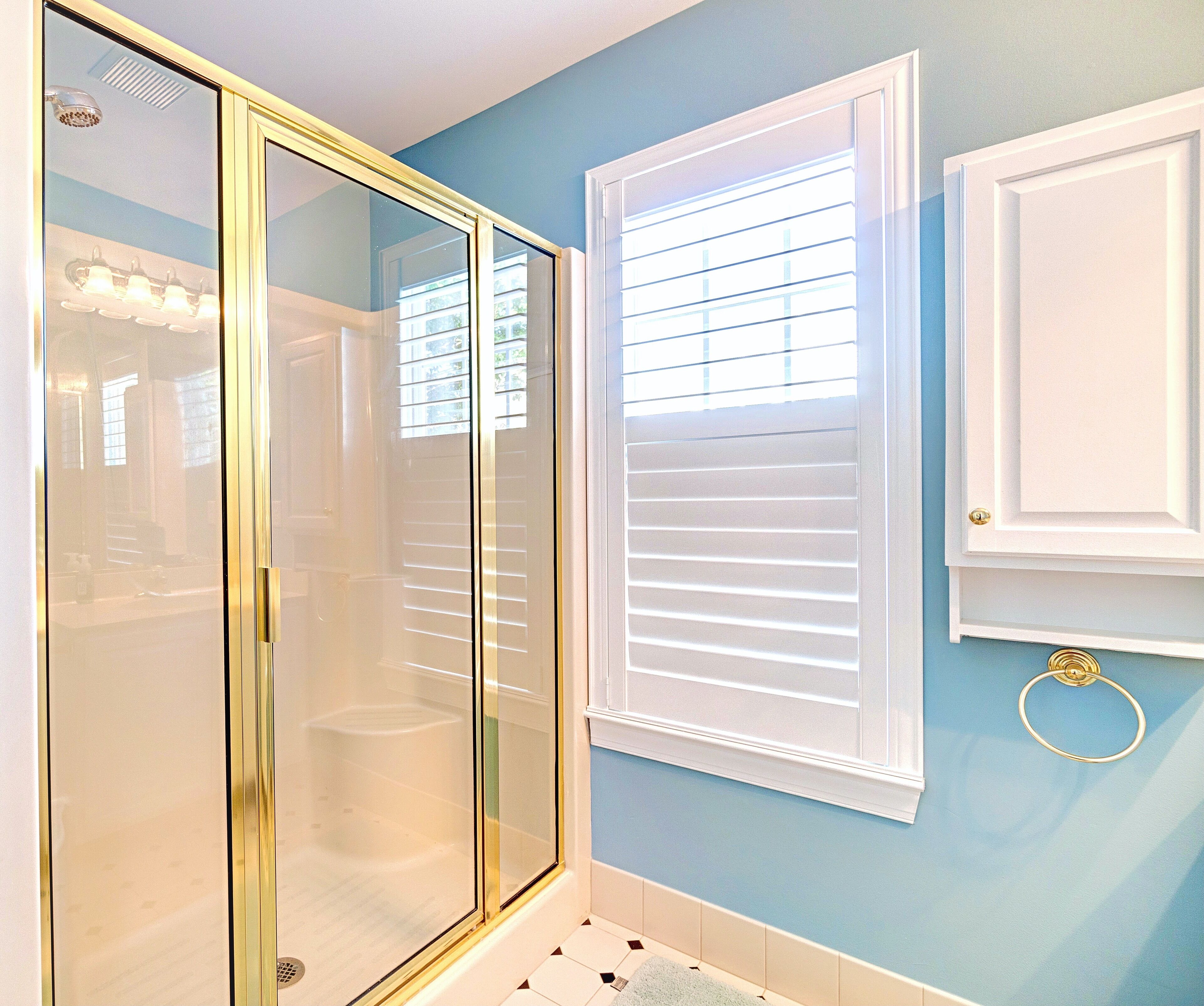 Un baño con cabina de ducha de vidrio, una ventana con persianas y un perchero para toallas.