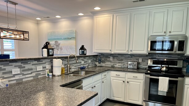 A modern kitchen with white cabinets, granite countertops, stainless steel appliances, and a tiled backsplash. - Guest-Favorite Rehoboth Beach Retreat:10/10 Reviews - Book early! (Rehoboth Beach)