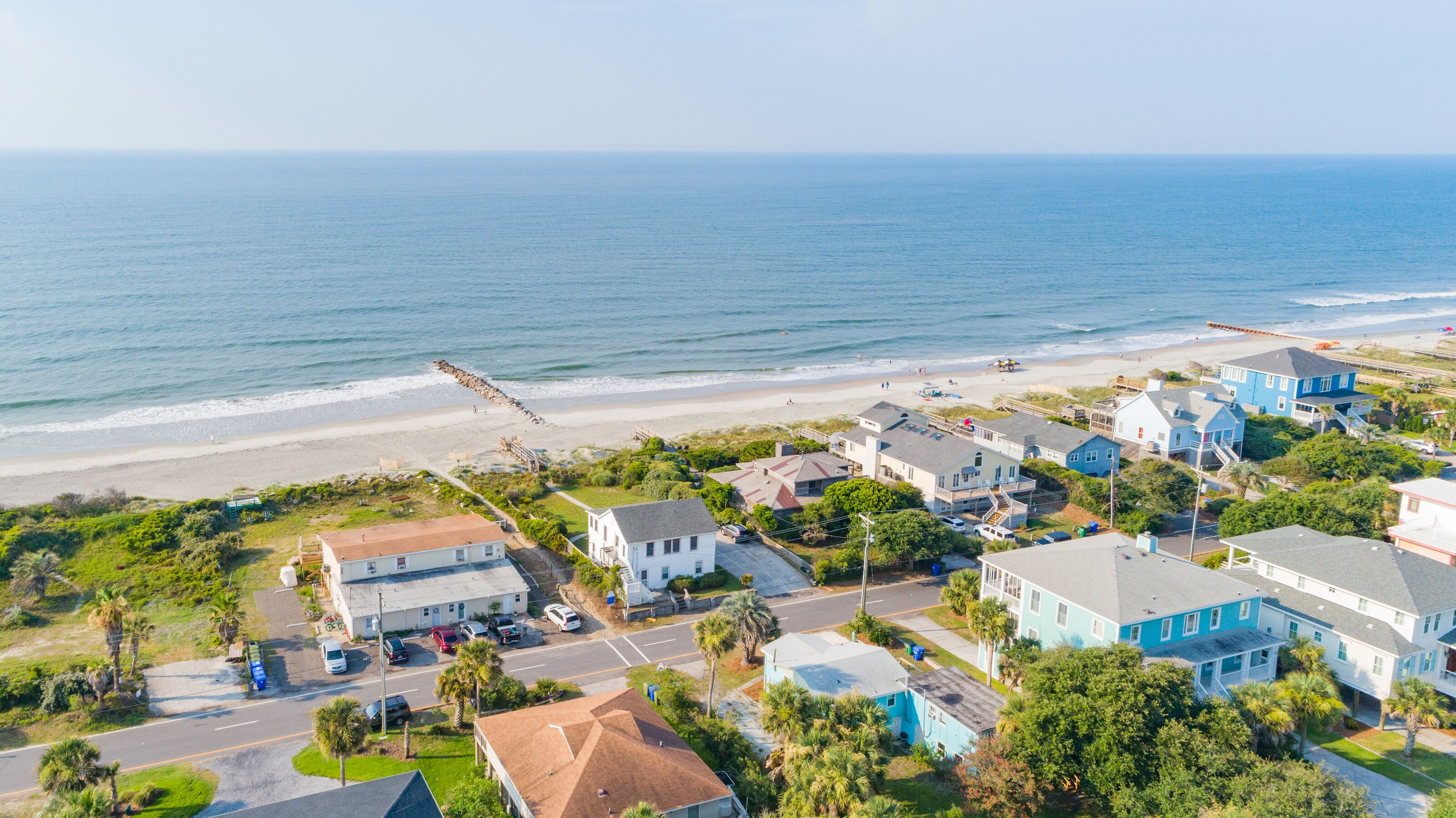 Vista aérea de una zona residencial costera con casas, una playa y un rompeolas rocoso.