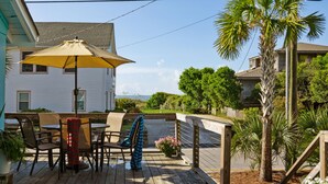 Una terraza de madera con mobiliario exterior, un paraguas amarillo y una palmera.