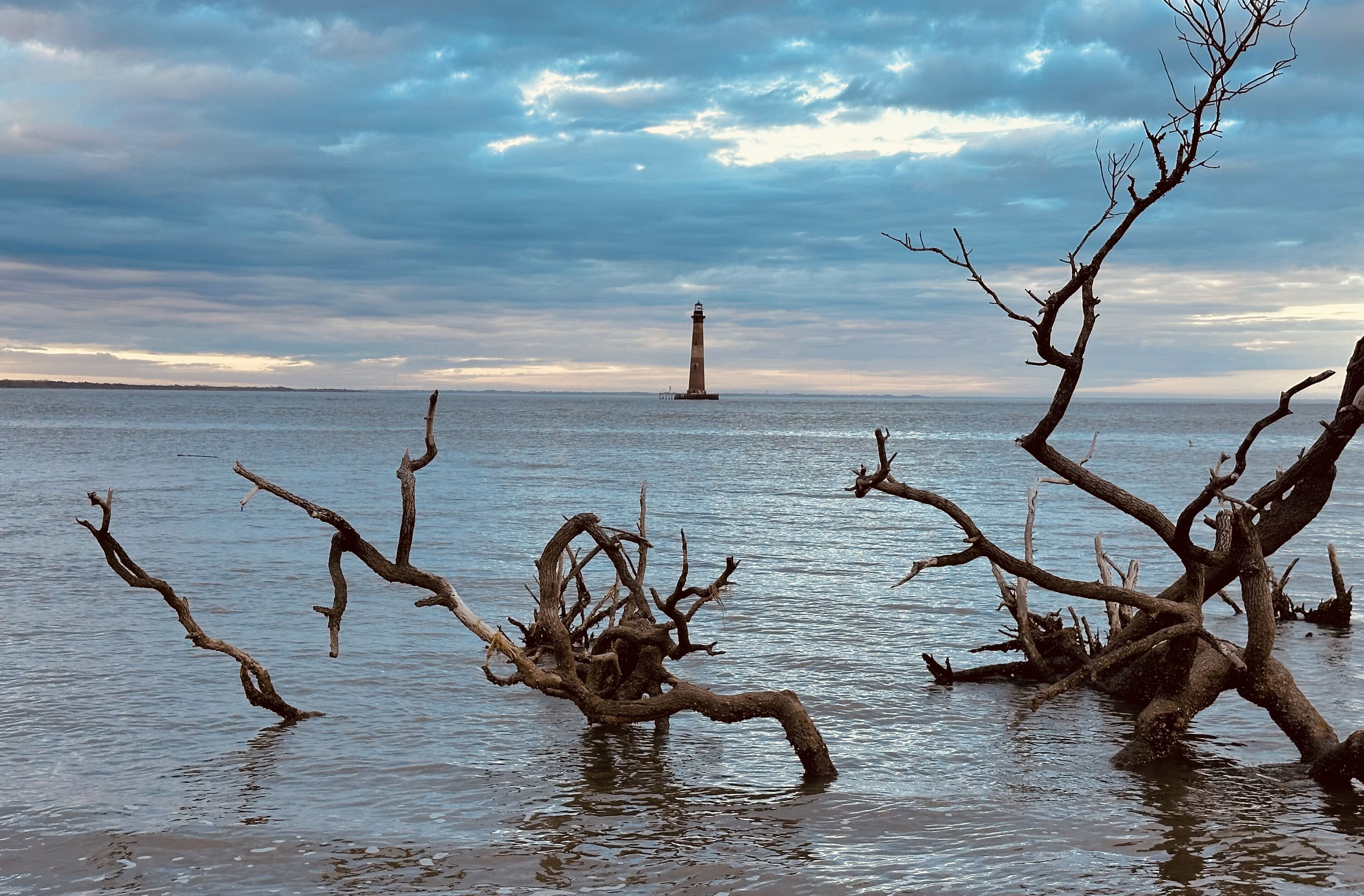A lighthouse on a small island in the distance, surrounded by calm water and overcast sky.