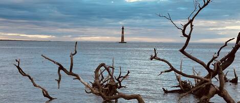 A lighthouse on a small island in the distance, surrounded by calm water and overcast sky.