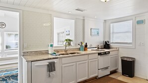 Una cocina moderna con gabinetes blancos, un lavamanos de acero inoxidable y un cubo de basura negro.