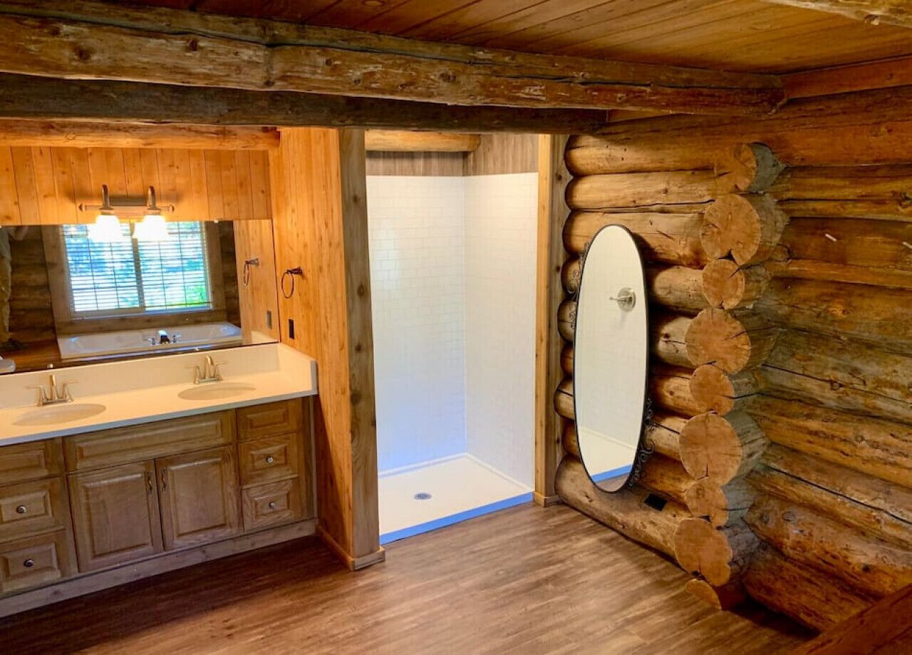 A log cabin bathroom with a wooden vanity, a large mirror, and a shower area.