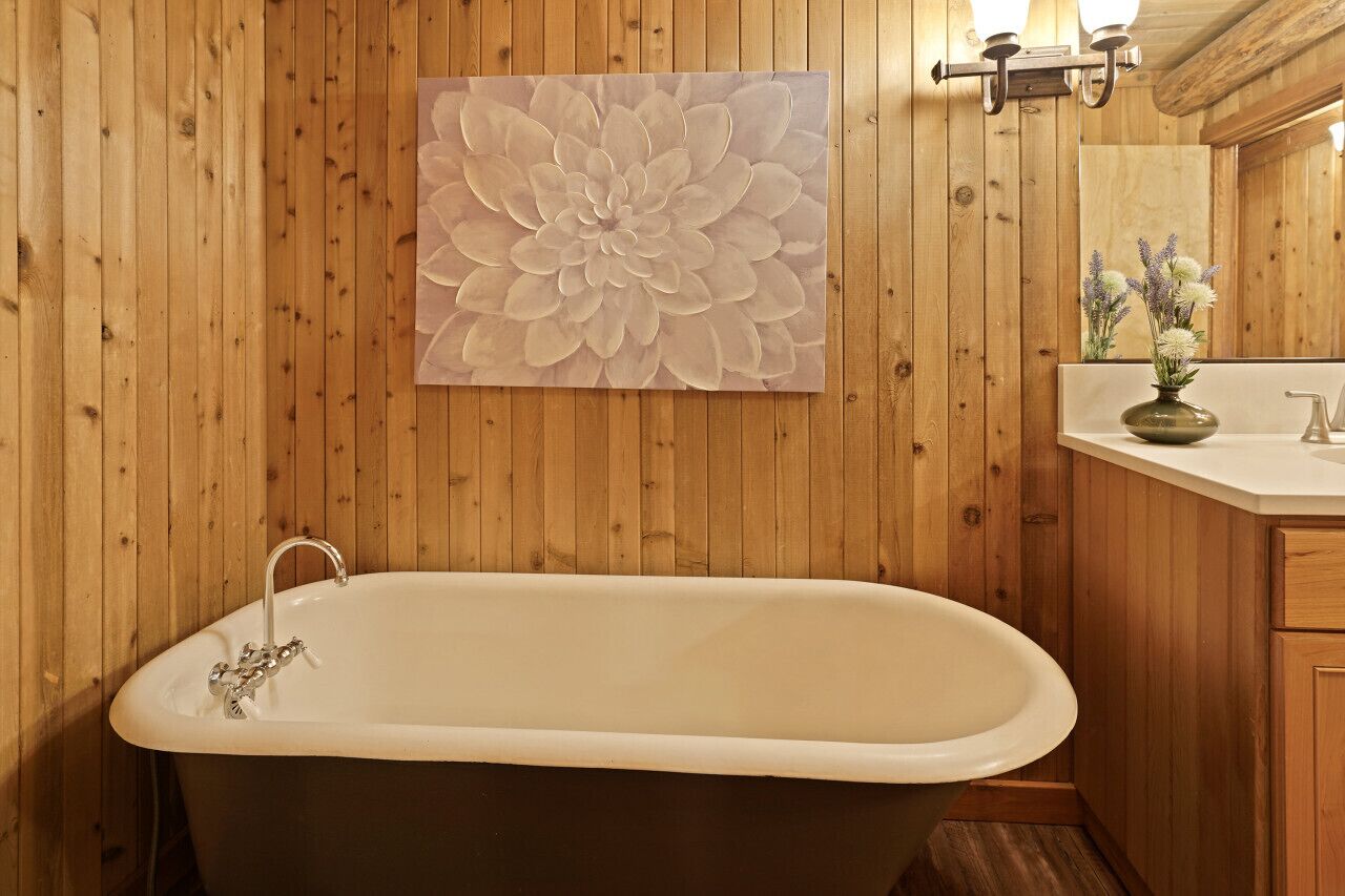 A wooden-paneled bathroom with a freestanding bathtub, a large floral artwork on the wall, and a small sink with a vase of flowers.