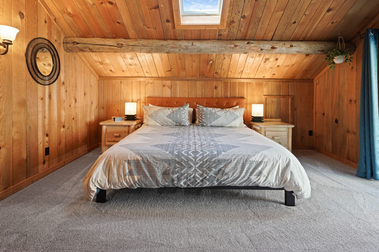 Een gezellige slaapkamer met een houten plafond, een groot bed met beddengoed met een patroon, twee nachtkastjes en een dakraam.