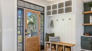 Una entrada moderna con puerta de madera, un banco, un estante pequeño con cestas, y un banco con bolsas tejidas.