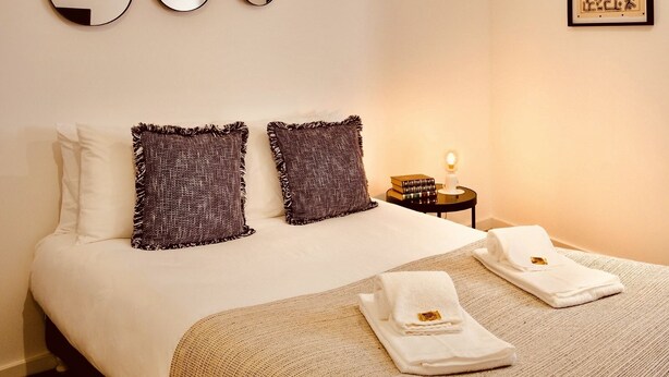 Habitación de hotel con una cama, dos almohadas, una mesita de noche con lámpara y tres espejos en la pared.