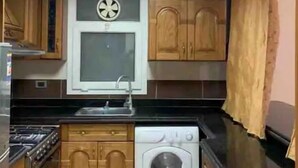 Eine kleine Küche mit Holzausstattung, einer integrierten Waschmaschine, einem Fenster mit Rundbogen und einer Deckenleuchte.