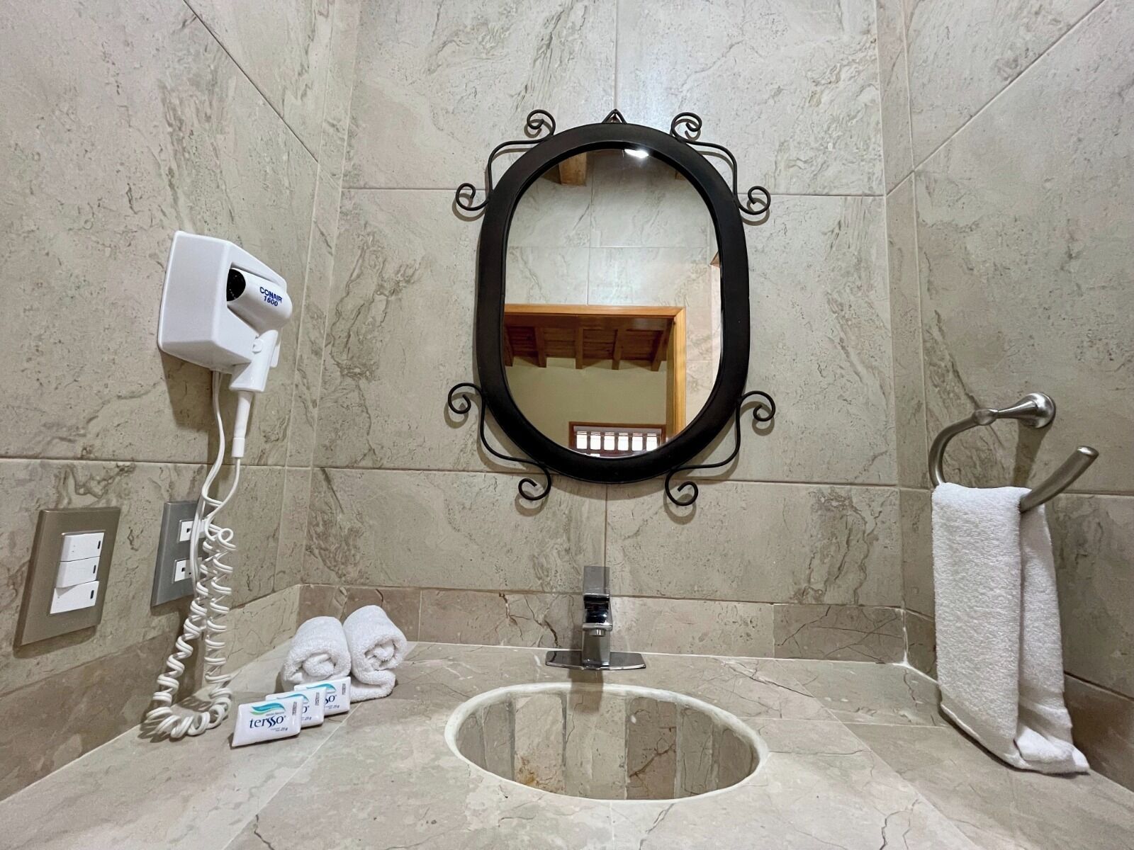 A bathroom with a marble sink, a black-framed mirror, a towel rack with a white towel, and a hairdryer on the wall.