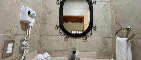 A bathroom with a marble sink, a black-framed mirror, a towel rack with a white towel, and a hairdryer on the wall.