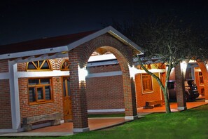 A brick building with a covered patio area, a carport, and a tree in front.