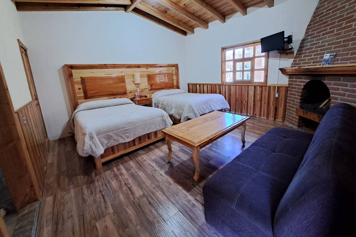 Una habitación con dos camas de madera, una mesa de madera, un sofá azul y una chimenea de ladrillo.