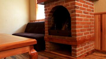 A brick fireplace with a wooden mantel, a wooden table, and a dark-colored sofa in a room with wooden flooring.