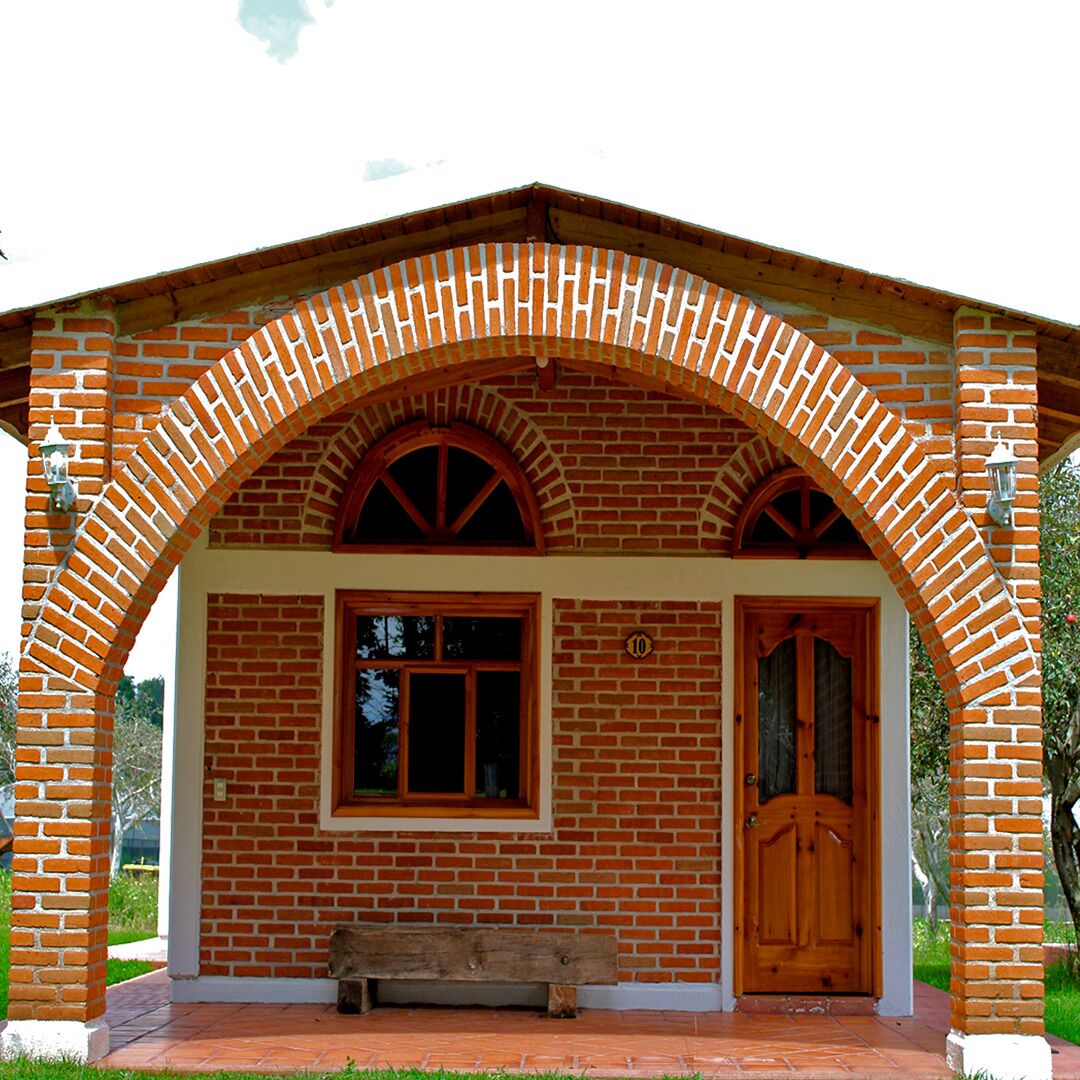 Un edificio de ladrillo con puerta y ventanas de madera, un banco en frente, y el número '10' en la pared.